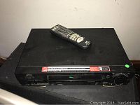 JVC VHS ET player with remote on top, black, dusty with power button on left side.