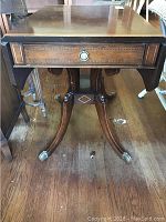 Front and side view of antique Duncan Phyfe style table showing hardwood surface, inlay detail, porcelain knob drawer, and claw feet on casters.