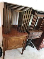 Four wooden nesting tables stacked on top of antique wooden cabinet showing tops and legs.