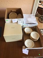 Boxes containing multiple stacks of Lenox china plates and saucers with gold rims, partially unboxed.