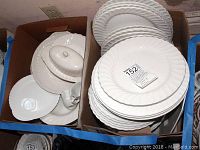 Two boxes filled with white plates and other dishware pieces, some plates stacked on top showing varying diameters