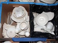 Overview of most items including plates, cups, sugar bowl, and salt and pepper shakers placed in two boxes, some broken pieces visible