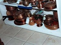 Shelf with various copper pots, pans, plates, and vases showing the assortment of the lot.