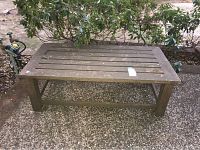 Overview of outdoor wooden table showing rectangular slatted top and weathered surface with dirt and debris.