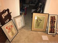 Four framed wall art pieces leaning against the wall and furniture, showing variety of subjects including flowers, botanical sketch, stylized bird, and totem print.