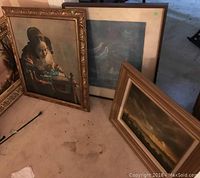 Three framed artworks leaning on floor: a detailed classical portrait, a sunset landscape print, and an original landscape painting by Adriaan Van Hofton.