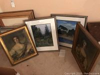 Four framed artworks grouped together on floor, two giltwood framed portraits of grand ladies and two framed landscape artworks by Freude in neutral frames.