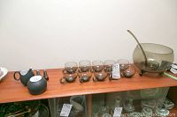 Overview of punch bowl set, six glass punch cups, cream and sugar set, pitcher, and salt and pepper shakers on wooden shelf.
