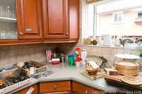 Corner kitchen countertop with flatware in boxes, knives, condiment containers, popcorn containers, wooden spoons, plate with lid and coasters near a window.