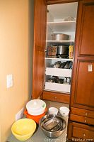 Photo of open kitchen cabinet containing various kitchen utensils including graters, pans, and slow cooker.