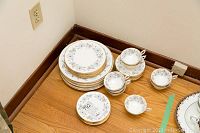 Full set of plates, teacups with saucers arranged showing the floral and gold design.