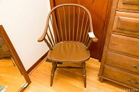 Full view of the brown painted Windsor style chair with spindle back and armrests positioned on hardwood floor.