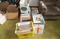 Multiple plastic crates and boxes containing various vinyl LP records including classical and popular music titles. Records stored upright and stacked, visible wear on sleeves.