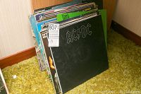 Photo of stack of vinyl LP records including AC/DC front cover with visible wear on sleeves.