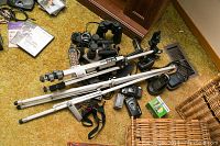 Overall view of the lot showing tripods, camera body, binoculars, cordless phones, and other items on a gold-colored carpet.