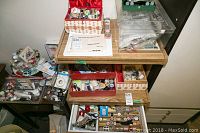 Wide shot of three wooden and woven boxes on a wooden table filled with various sewing items including thread spools, buttons, needles and measuring tape.