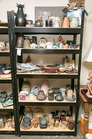 Shelf unit with pottery and ceramic items arranged on multiple levels showcasing variety and condition.