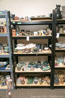 Photo showing black metal shelving unit filled with assorted decorative ceramics and pottery items on four shelves