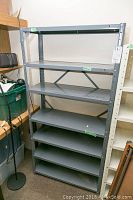 Full view of gray metal utility shelf with six shelves, note writing visible.