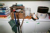 Wide shot of the collection on white cabinets including umbrellas hanging on edge, wooden shoe shine kit, shoe stretchers, walking sticks, stoneware crock, and metal milk can