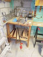 Full view of wooden work table holding ball bearing grinder, clamps, T-squares, and wood pieces.
