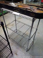 Side angle showing two-tier chrome wire utility shelf with metal tubing legs and wire grid shelves.