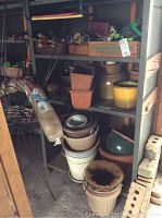 Shelf with multiple stacked ceramic and clay plant pots in different sizes, stacked planters, and some cans.