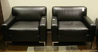 Pair of black faux leather armchairs with chrome-finish square legs viewed from the front