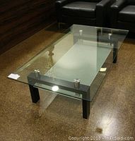 Front angle view of the rectangular glass coffee table showing the clear glass top with metal supports and black legs.