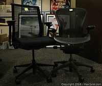 Two black mesh office chairs side by side in office setting