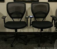 Pair of two black office chairs with mesh backs and padded seats, side by side on carpeted floor.