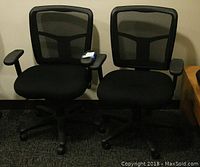 Pair of black office chairs with mesh backs, padded seats, and rolling bases shown side by side.