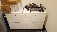 White 4-drawer metal file cabinet with four drawers, handles, and a flat top surface with office supplies on top.