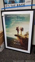 Framed 'Walk in the Woods' movie poster showing two men on a cliff with nature background, in a black frame with visible wear on the glass.