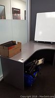 Photo of office workstation desk with cardboard box containing mesh trays on top, and whiteboard on stand to the right