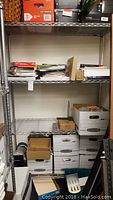 Full view of wire rack with multiple boxes and stacks of paper, binders, and office supplies.