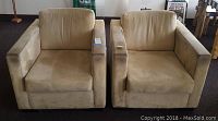 Two beige microsuede armchairs seen from front, showing boxy design with square arms and removable cushions.