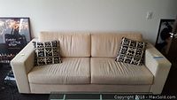 Front view of the beige fabric sofa with two black and white patterned pillows placed on the cushions.