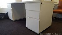 Side view of white work desk showing three drawers and wear on surface and edges.