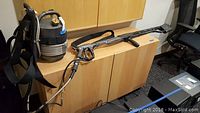 Full view of flame thrower prop showing backpack tank with straps and connected long gun nozzle on display surface.