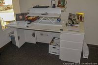 White office desk with three drawers on the right and open space on the left, visible wear and stains, raised platform on top, office items around.