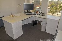 L-shaped desk with computer monitor, keyboard, telephone, and other office accessories on top, showing the full structure and drawer placement.
