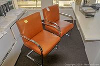 Two orange leather office chairs with chrome sled metal frames in an office environment.