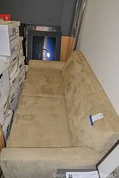 Beige fabric sofa with straight arms and a suede-like texture, positioned against the wall near boxes.