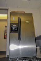 Full view of the stainless steel Kenmore side-by-side refrigerator with black handles and water/ice dispenser on left door.