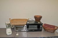 Wide view of all items: blender, toaster oven, microwave, and baskets on flat surface.