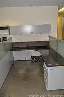 Office cubicle workspace showing dark laminate work surface with glass panel dividers and lockable overhead metal cabinets