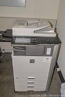 Front view of copier showing control panel, digital display, paper exit and three lower paper trays