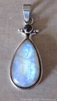 Front view showing the pear-shaped rainbow moonstone with blue opalescence and round garnet cabochon above, set in sterling silver pendant with bail.