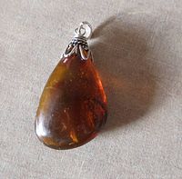 Close-up of the amber pendant lying flat showing the polished amber surface with internal inclusions and the sterling silver setting attached to the top.